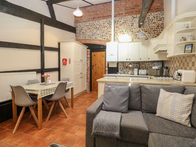 An open kitchen and dining area with a wooden table and gray chairs and a gray sofa at Hitchens Cottage in Happisburgh