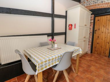 A dining table with four chairs a patterned tablecloth and flowers in a kitchen at Hitchens Cottage in Happisburgh
