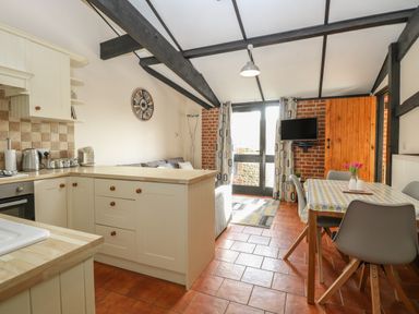 A kitchen and dining area with a wooden table and chairs a sofa and television at Hitchens Cottage in Happisburgh