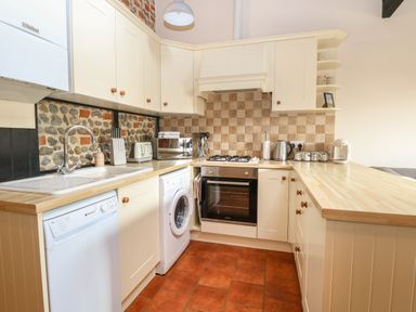 A kitchen with white cabinets wooden countertops washing machine dishwasher oven and tiled backsplash at Hitchens Cottage in Happisburgh