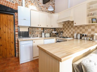 A kitchen with wooden countertops white cabinets tiled floor and brick and stone walls at Hitchens Cottage in Happisburgh