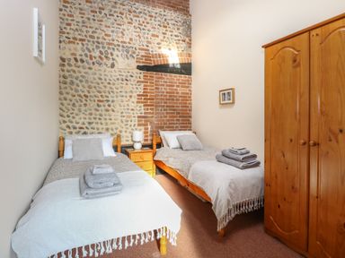 A bedroom with two single beds a wooden wardrobe and a stone and brick wall at Hitchens Cottage in Happisburgh