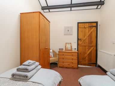 A bedroom with two single beds wooden wardrobe wooden chest of drawers and a wooden door at Hitchens Cottage in Happisburgh