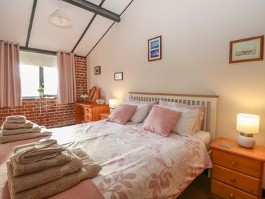 A bedroom with a double bed pink pillows towels on the bed nightstand with lamp and framed pictures on wall at Hitchens Cottage in Happisburgh