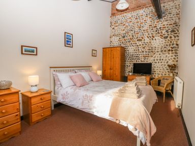 A bedroom with a double bed wooden furniture and a stone accent wall at Hitchens Cottage in Happisburgh