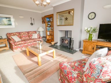 A living room with a patterned sofa and armchair a wooden coffee table a fireplace a wooden bookshelf and a television at Kirkstone Cottage in Outgate near Hawkshead