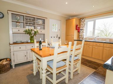 A kitchen dining area with wooden table and chairs near cabinets and a cupboard at Kirkstone Cottage in Outgate near Hawkshead