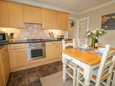 A kitchen with wooden cabinets a stove and a dining table with four chairs and flowers at Kirkstone Cottage in Outgate near Hawkshead