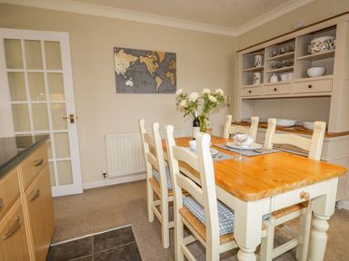 A dining area with a wooden table and six chairs cushions flowers and tableware a cabinet with dishes and glassware a wall map at Kirkstone Cottage in Outgate near Hawkshead