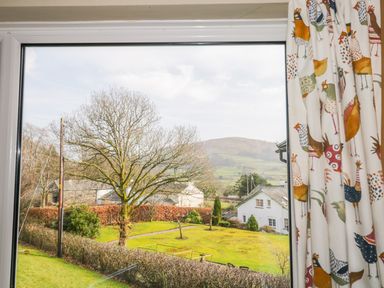 A window view showing a garden with trees bushes and houses with hills in the background at Kirkstone Cottage Outgate near Hawkshead