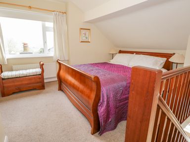 A bedroom with a wooden bed covered with a purple bedspread a wooden bench under a window and a framed picture on the wall at Kirkstone Cottage in Outgate near Hawkshead
