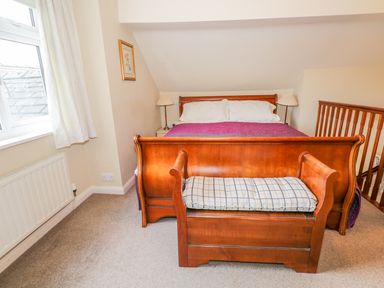 A bedroom with a wooden bed and a bench at the foot of the bed with a cushion at Kirkstone Cottage Outgate near Hawkshead