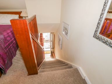 A staircase with wooden railing leading down from a bedroom with a bed and lamp at Kirkstone Cottage in Outgate near Hawkshead