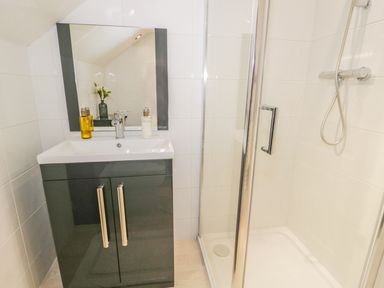 A bathroom with a sink, mirror, soap dispenser, and a shower with glass door at Kirkstone Cottage in Outgate near Hawkshead