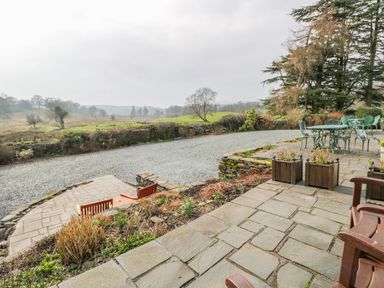 An outdoor patio with stone flooring wooden benches metal table and chairs overlooking a gravel path and fields at Kirkstone Cottage Outgate near Hawkshead
