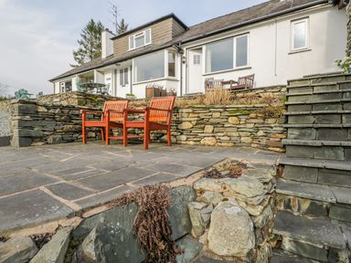 An outdoor stone patio with wooden benches stone steps and a white house in the background at Kirkstone Cottage in Outgate near Hawkshead