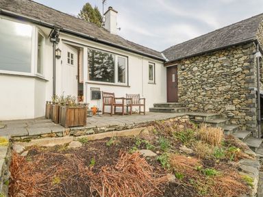 An outdoor patio area with two wooden chairs a small table wooden planters and stone steps at Kirkstone Cottage in Outgate near Hawkshead