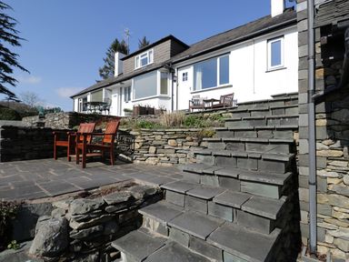 An outdoor patio with stone steps and wooden chairs in front of a white house at Kirkstone Cottage in Outgate near Hawkshead