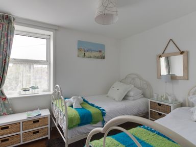 A bedroom with two single beds side by side with striped blankets and pillows a window with floral curtains and wicker storage drawers at Fenders Brewers Quay Harbour