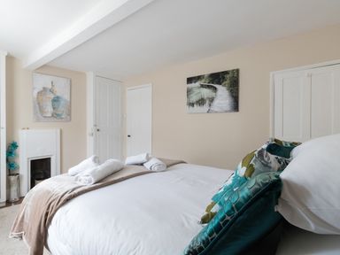 A bedroom with a bed with white sheets and rolled towels two paintings on beige walls and two closed white doors at Fenders Brewers Quay Harbour