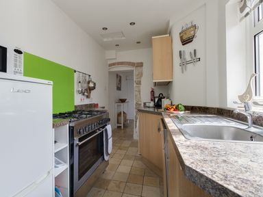 A narrow kitchen with a stove refrigerator sink countertop and utensils hanging on the wall at Fenders Brewers Quay Harbour