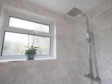 A tiled shower area with a window and a potted plant on the windowsill at Fenders in Brewers Quay Harbour