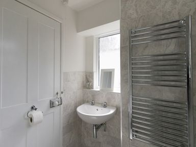 A bathroom corner with a white sink under a frosted window and a chrome towel radiator at Fenders Brewers Quay Harbour