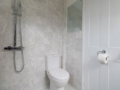 A bathroom with a toilet, wall-mounted shower, tiled walls, and a door with a toilet paper holder at Fenders Brewers Quay Harbour