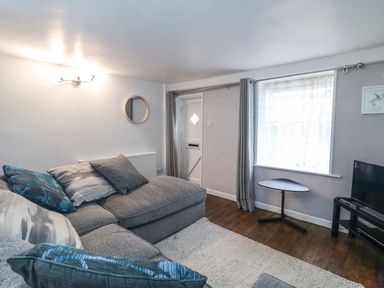 A living room with a gray sectional sofa gray curtains a small black table a wall-mounted light and a window at Fenders in Brewers Quay Harbour