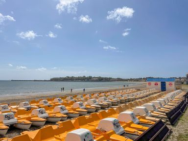 Rows of yellow and white pedal boats on a beach near water and a pier at Fenders in Brewers Quay Harbour
