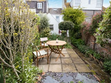 A garden patio with two wooden chairs and a table surrounded by plants and trees at Fenders in Brewers Quay Harbour