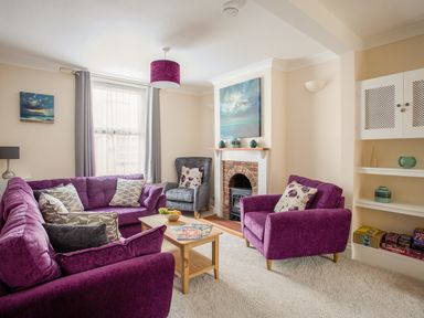 A living room with purple sofas and armchair a fireplace and wooden coffee table at Wey Cottage in Weymouth