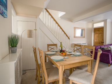 A dining area with a wooden table set for four near a staircase and a living room with a purple sofa at Wey Cottage in Weymouth