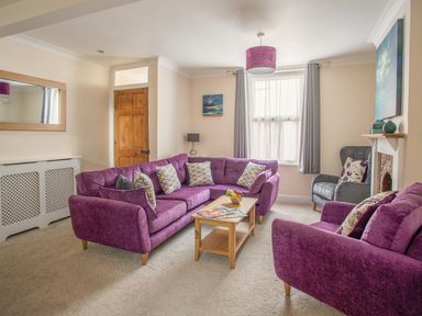 A living room with purple sofas a wooden coffee table a grey armchair and a window at Wey Cottage in Weymouth