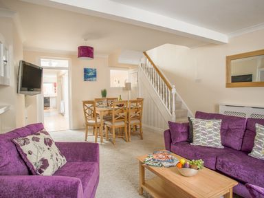 A living room with purple sofas a wooden dining table with chairs and a staircase at Wey Cottage in Weymouth