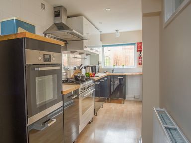 A narrow kitchen with black and white cabinets a built in oven a stove a window and a fire extinguisher at Wey Cottage in Weymouth