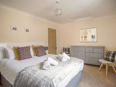 A bedroom with a bed with pillows and rolled towels a gray dresser two chairs and a mirror at Wey Cottage in Weymouth