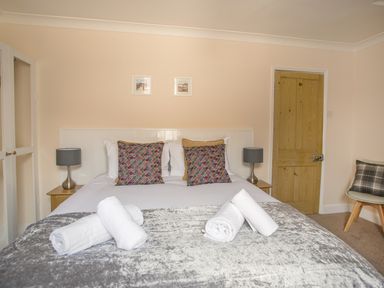 A bedroom with a double bed with patterned cushions and rolled white towels a wooden door and a chair with a plaid cushion at Wey Cottage Weymouth