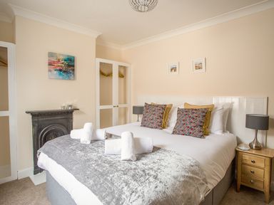 A bedroom with a double bed with patterned cushions and rolled towels beside a wooden nightstand and fireplace at Wey Cottage in Weymouth