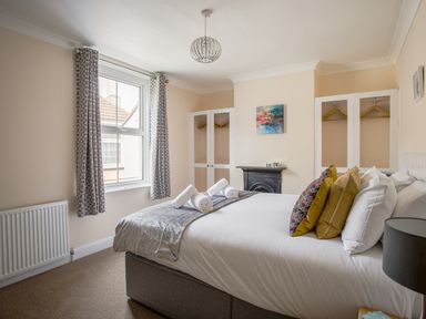 A bedroom with a bed with decorative pillows and rolled towels near a window and built-in wardrobes at Wey Cottage in Weymouth