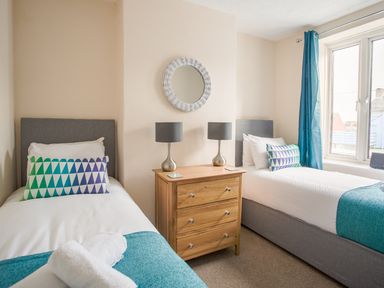 A bedroom with two single beds a bedside table with two lamps and a window at Wey Cottage in Weymouth