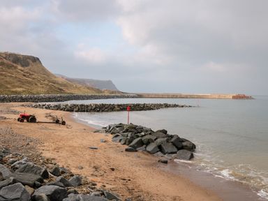 A sandy beach with rocks and a red tractor near the shoreline and cliffs in the background at Lady Bird Retreat in Skinningrove