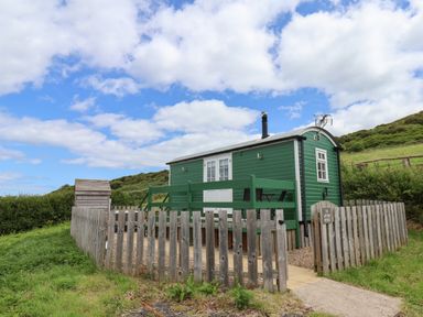 A small green wooden cabin with a fenced yard and chairs on a patio under a partly cloudy sky at Lady Bird Retreat in Skinningrove