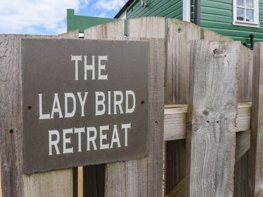 A wooden gate with a sign saying The Lady Bird Retreat and part of a green house visible in Skinningrove