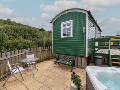 An outdoor patio with a green bench table and chairs a green wooden cabin a hot tub and a fence at Lady Bird Retreat in Skinningrove