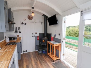 A kitchen area with wooden countertops a stove a kettle utensils a wood burning stove a wall clock a small wooden table on wheels and a door open to a porch at Lady Bird Retreat in Skinningrove