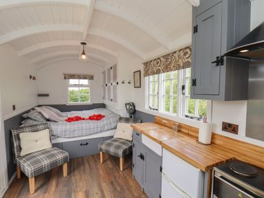A small living space with a bed, two plaid chairs, a wooden countertop, sink, and gray cabinets at Lady Bird Retreat in Skinningrove