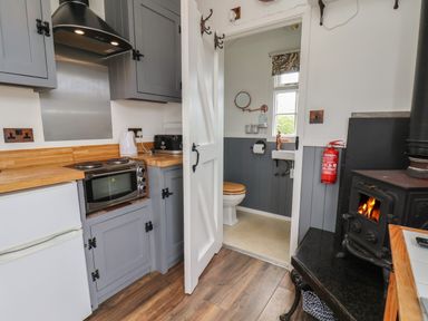 A kitchen with gray cabinets wood countertops a small oven and a white fridge next to a bathroom with a wooden toilet seat and a sink at Lady Bird Retreat in Skinningrove