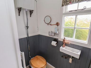A small bathroom with a toilet with a wooden seat a high cistern a wall-mounted sink and a frosted window at Lady Bird Retreat in Skinningrove
