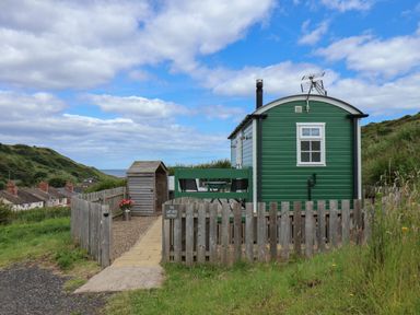 Green cabin with a fenced yard and a wooden shed near hill and houses at The Lady Bird Retreat in Skinningrove